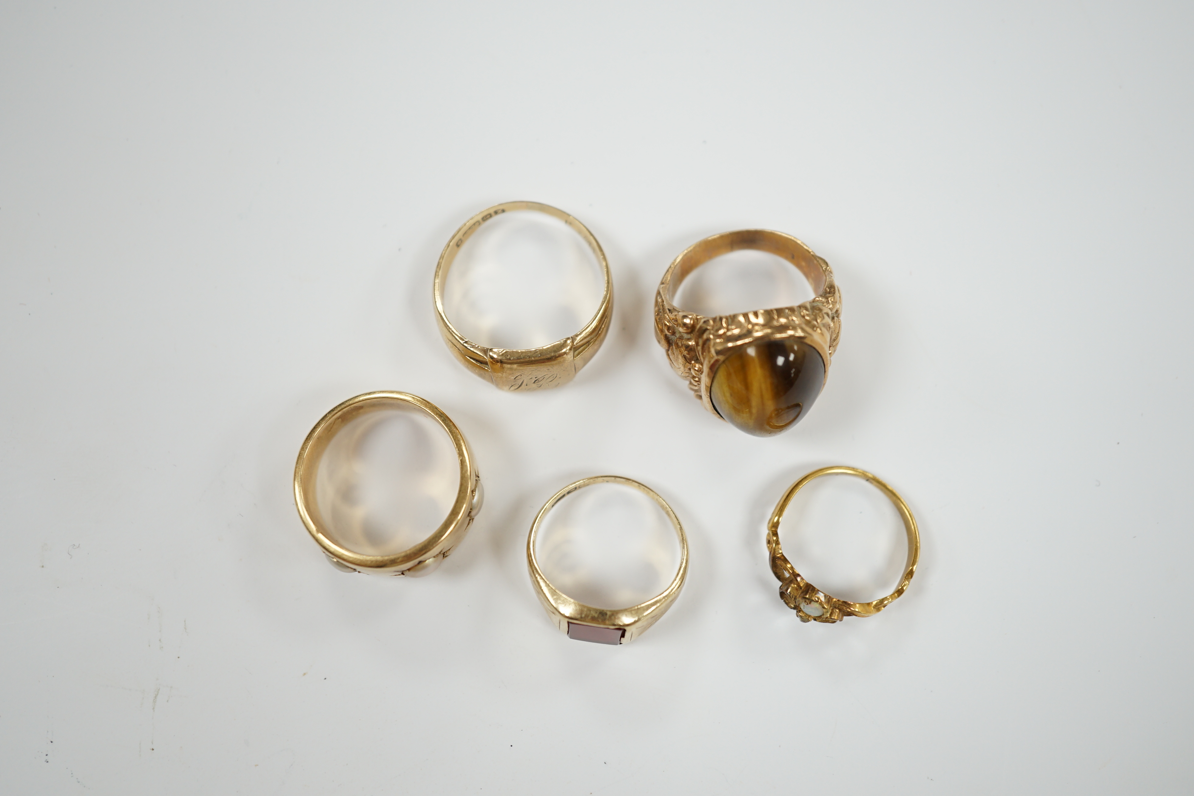 A 9ct gold signet ring, a gold and carnelian set signet ring and three yellow metal rings one set with three split pearls and one set with tiger's eye quartz cabochon, gross weight 29.7 grams.